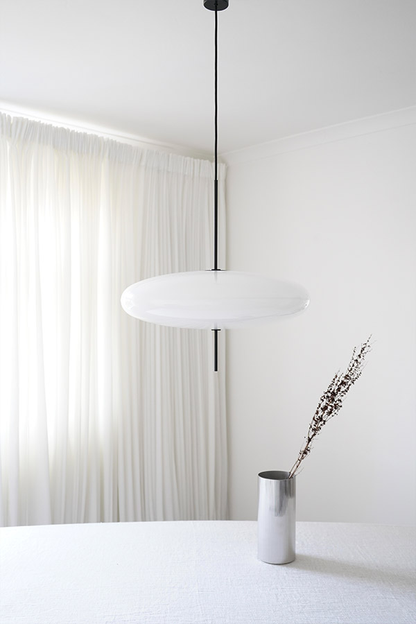 A minimal black and white pendant light above a white table and silver vase