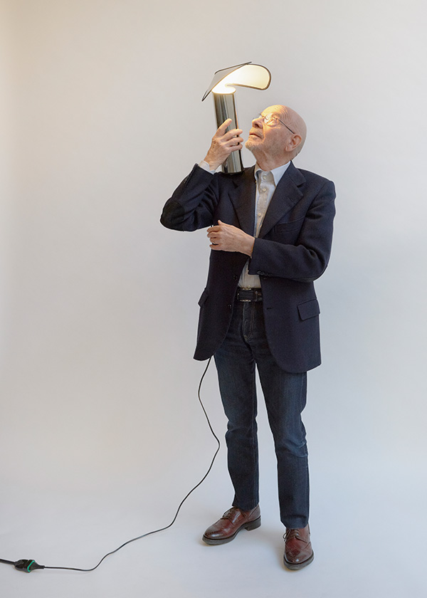 Mario Bellini with a small Chiara table lamp on his shoulder