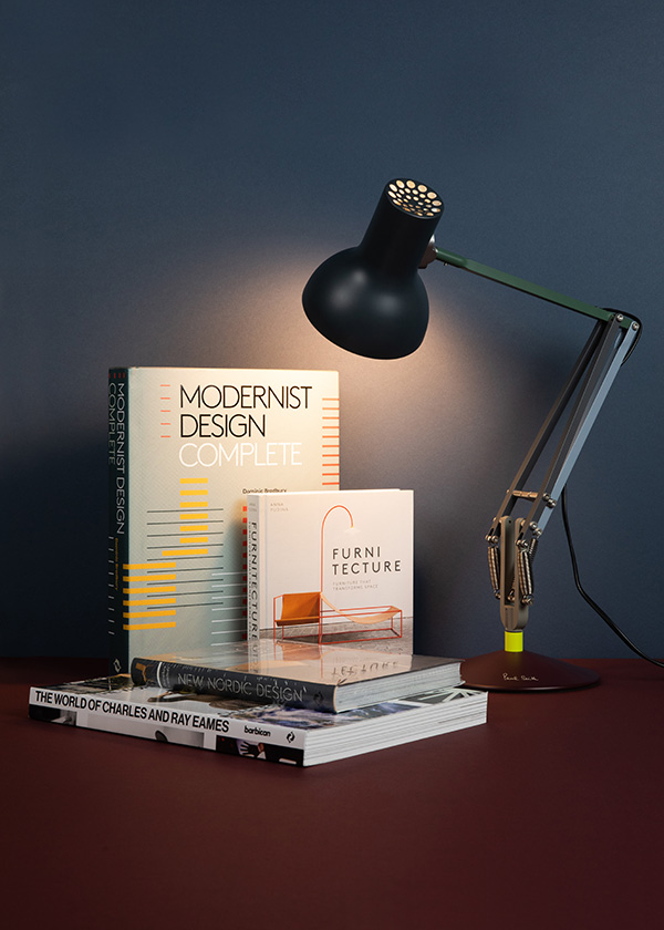 An Anglepoise lamp illuminating a stack of books against a coloured background