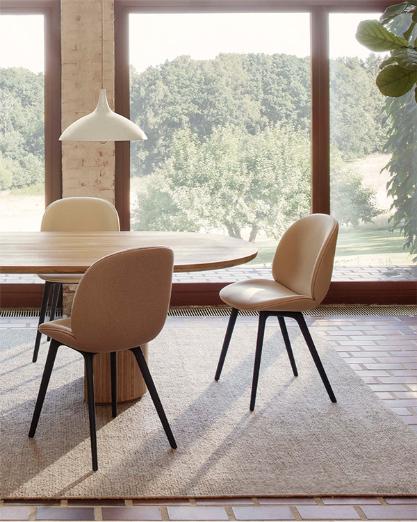 Neutral fabric Beetle chairs around a wooden dining table with a few of trees behind