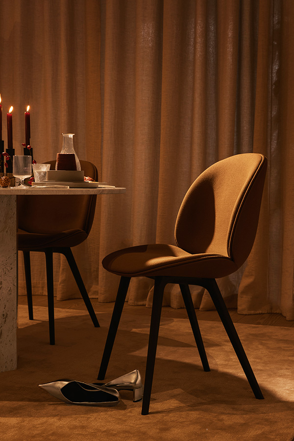 A fully upholstered Gubi Beetle Chair in burnt orange at a dining table