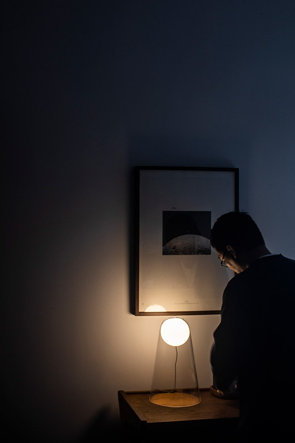 Man standing next to the Foscarini Satellite table lamp in a dark room