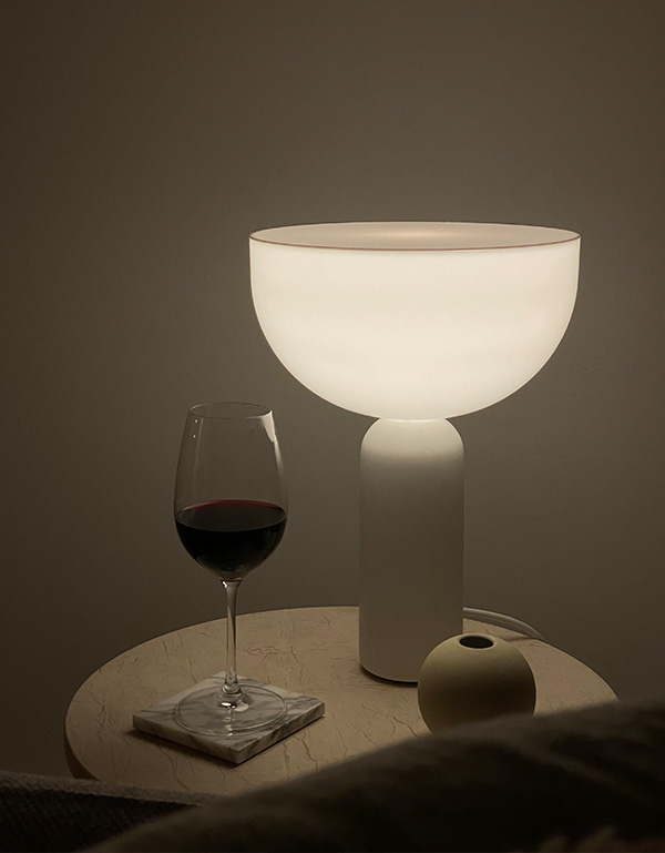 Glowing New Works Kizu table lamp next to a glass of red wine