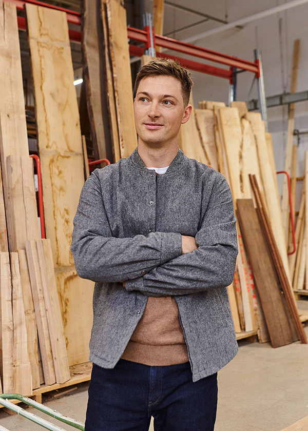 Designer Mathias Steen Rasmussen standing in front of wood planks in a factory