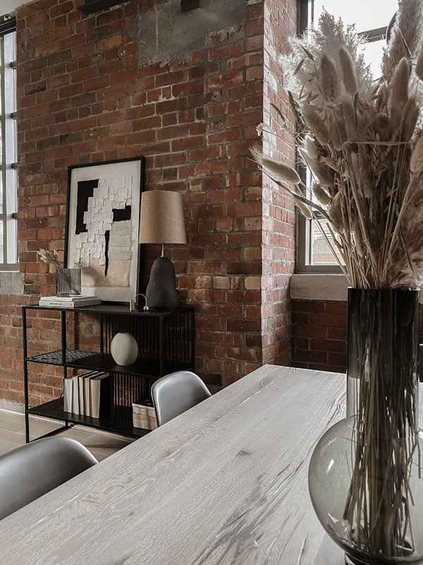 Looking from a dining table over to an exposed brick wall with shelving unit