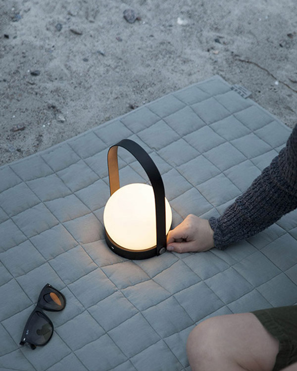 The Audo Copenhagen Carrie Portable LED Table Lamp on a picnic blanket