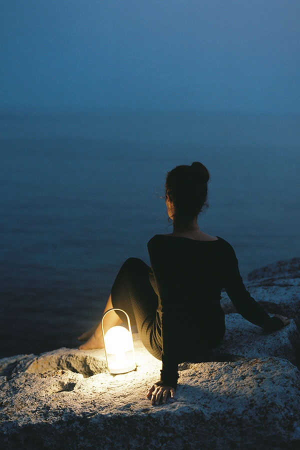 A Marset FollowMe portable lamp next to a woman sitting on rocks at night