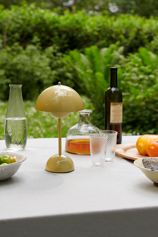 A yellow &Tradition VP9 portable table lamp on an outdoor dining table