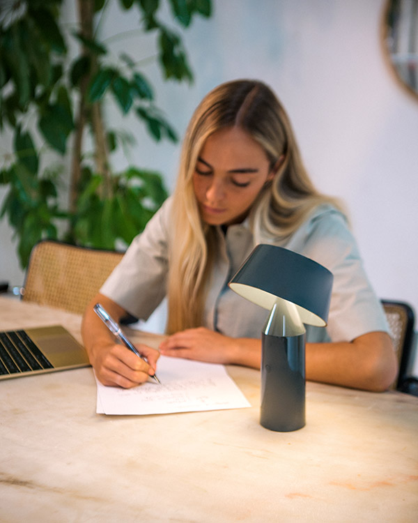 Marset Bicoca in blue next to a woman writing notes at a table