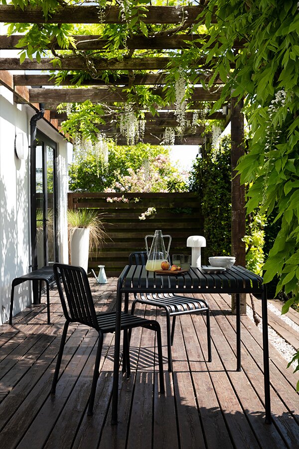 The Hay Palissade Outdoor Table and Chairs under a veranda with green climbing plants