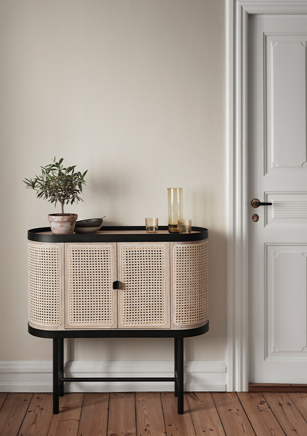 Warm Nordic Be My Guest Bar Cabinet next to a door, with a small plant on top and glasses