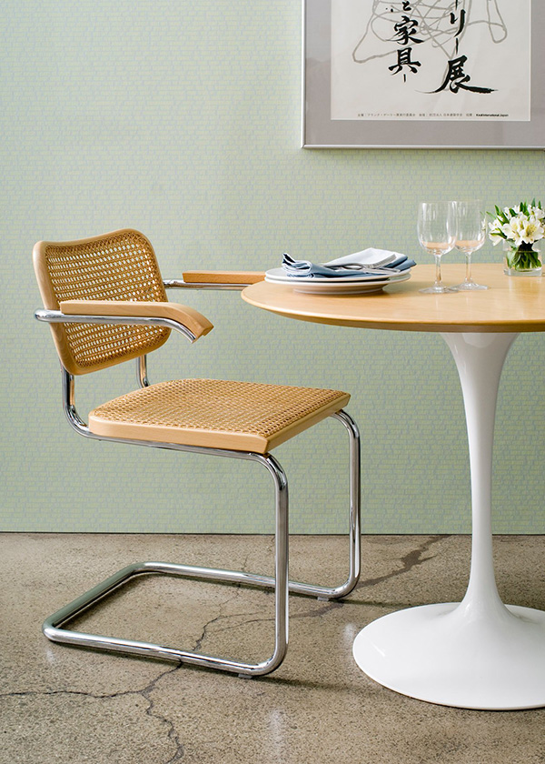 A wooden and rattan Knoll Cesca Chair next to a small Tulip Table