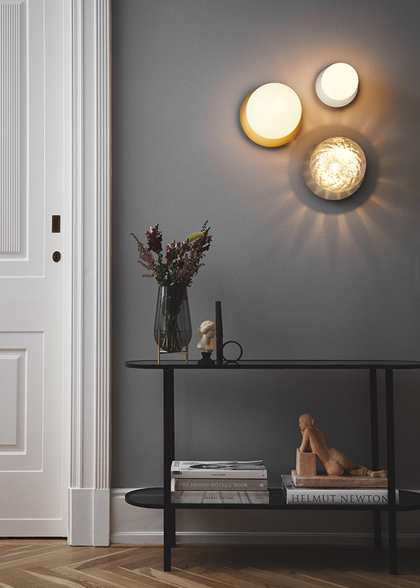 3 Nuura Liila wall lights on a dark grey wall above a shelving unit