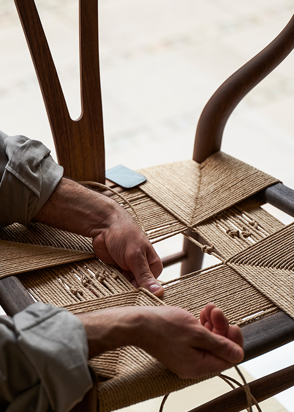 Someone weaving the seat of a CH24 wishbone chair