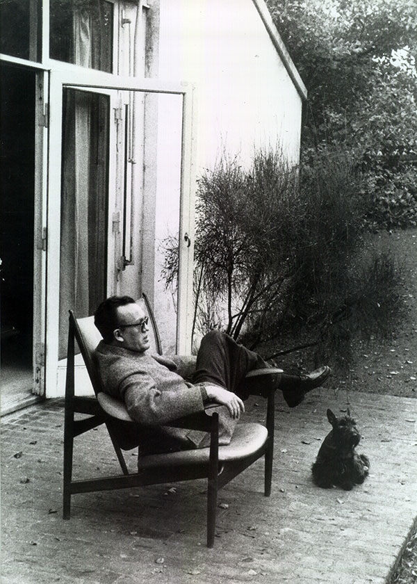 A black and white photo of Finn Juhl sitting in his Chieftain Chair in his garden