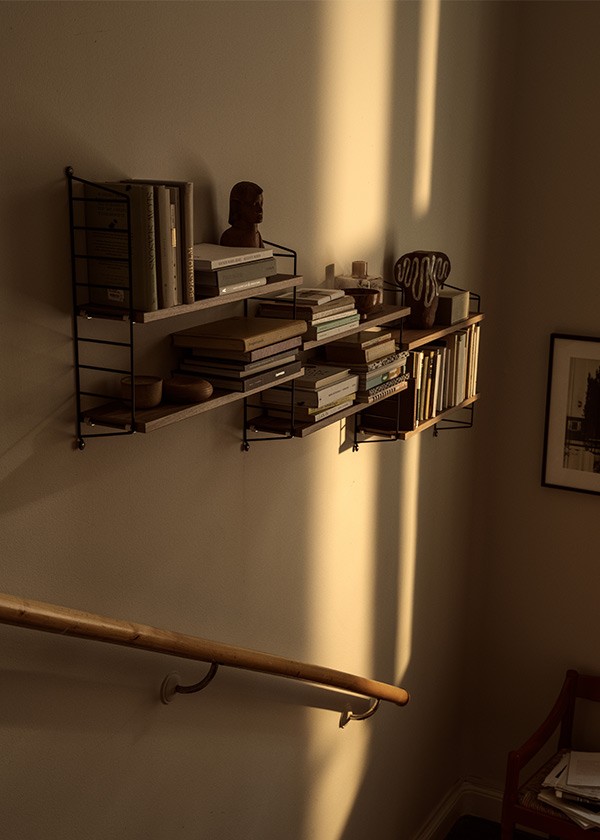 String Pocket wall shelving unit styled with books, ceramics and decorative objects, illuminated by warm sunlight in a modern interior.