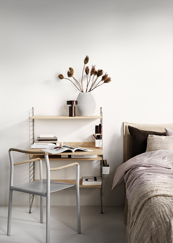 A string desk being used as a dressing table next to a bed
