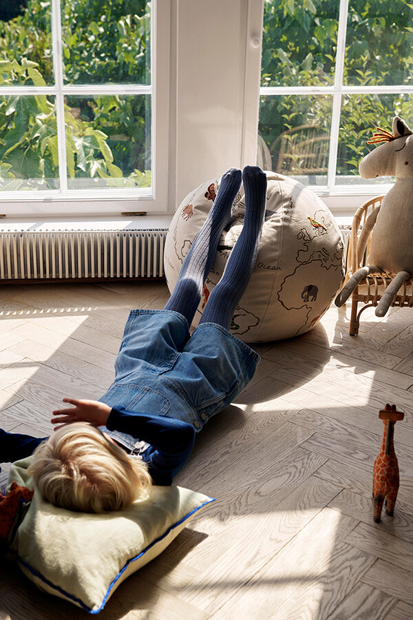 Child lying down with feet resting on ferm LIVING World Pouf