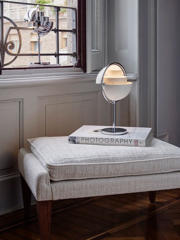 GUBI Multi-Lite Portable resting atop a footstool and coffee table book
