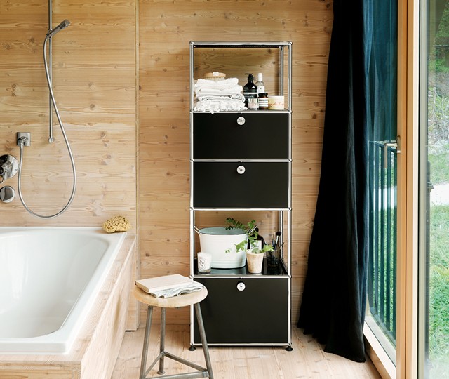 Black and chrome modular shelving unit with storage drawers and open shelves, styled with towels and toiletries in a wood-paneled bathroom next to a bathtub.