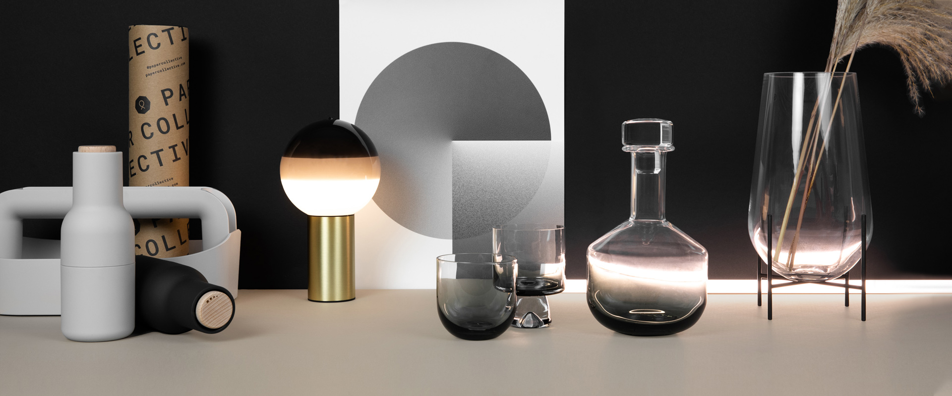 Monochrome backdrop with Marset Dipping Table Lamp - Portable, Paper Collective EO Shapes Print Collection 03, Tank Whiskey Decanter with Tank Low Ball Glasses, Menu Echasse Vase and Grinders. Image - Max Hawley