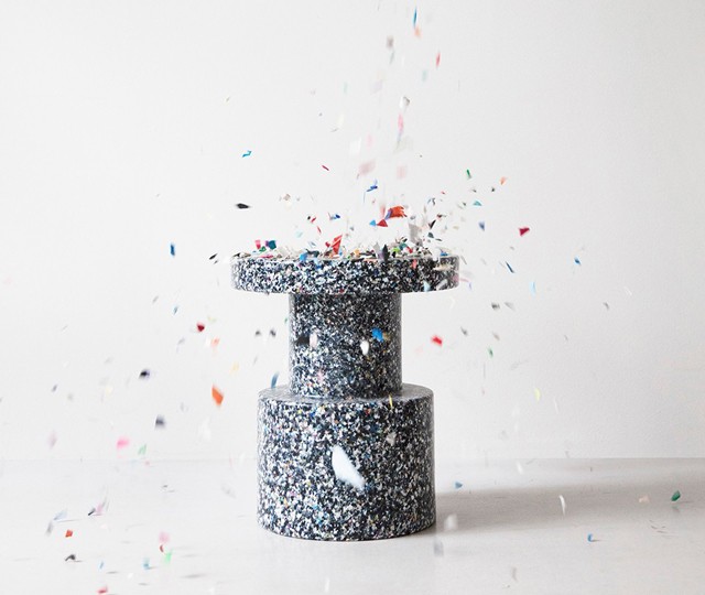 Speckled recycled plastic side table with colourful plastic flakes falling around it against a white background.