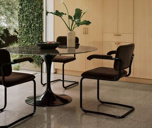 Black marble tulip dining table and dark brown velvet cantilever chairs on a terrazzo floor