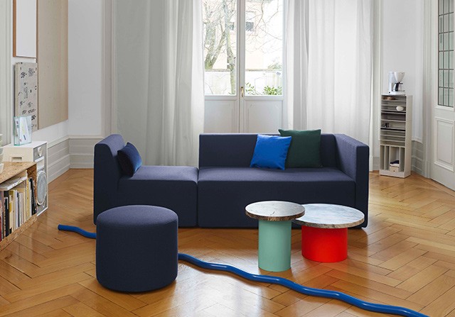 Modern dark blue modular sofa with colorful accent coffee tables on herringbone hardwood floors