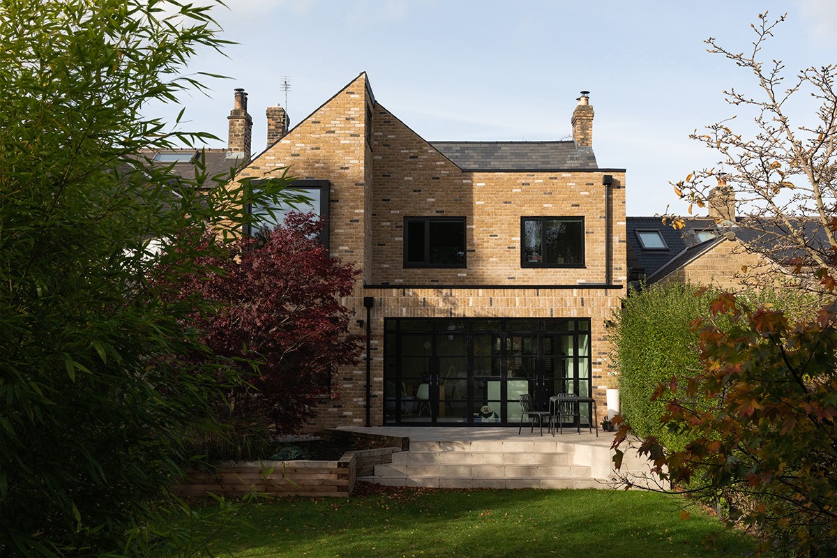 Contemporary two-story brick home extension featuring black window frames and a tiled patio leading to a lawn.