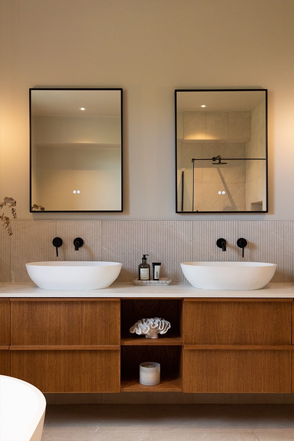 Modern bathroom vanity featuring two white oval counter basins, black fixtures, and two LED-lit framed mirrors.