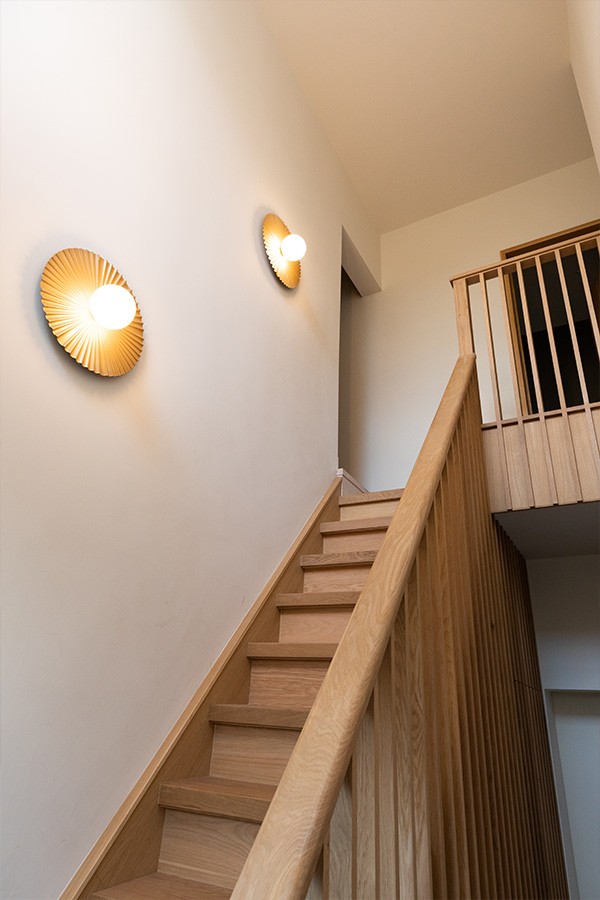 Light oak wooden staircase with vertical slat banisters, illuminated by glowing pleated wall sconces.