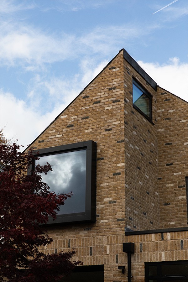 Large square black-framed picture window set in a textured brick wall beside a red maple tree.