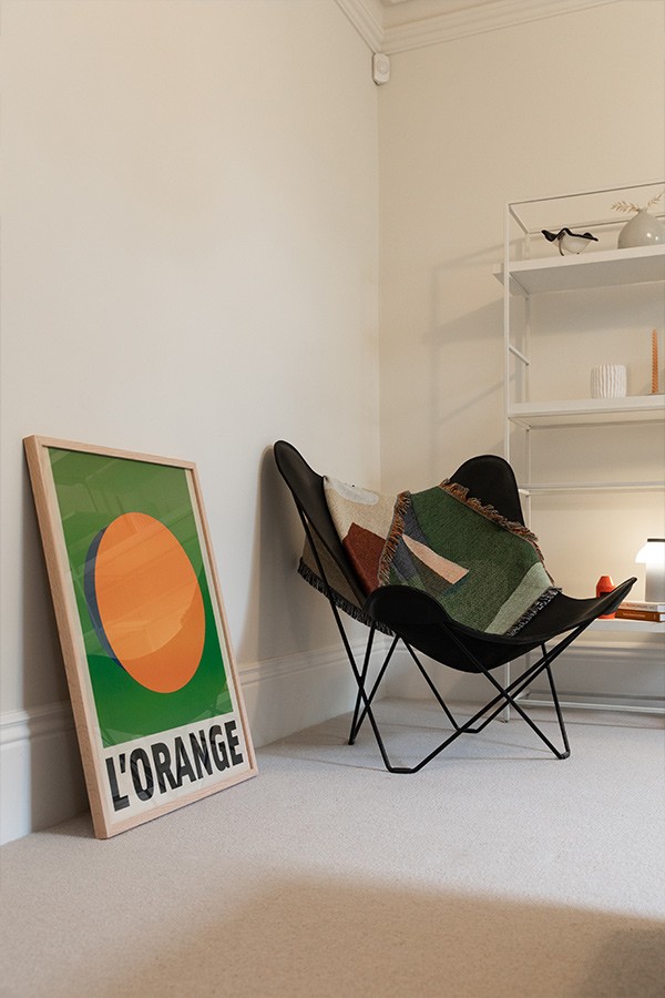 Minimalist corner setup with a black sling butterfly chair, green and orange art print, and white shelving unit.