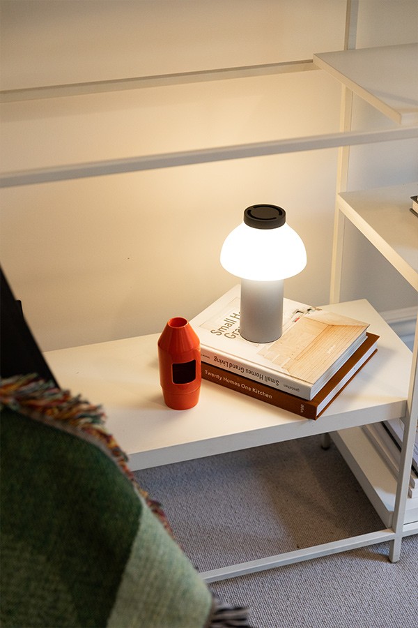 White shelving unit decorated with a small glowing portable table lamp, books, and an orange diffuser.