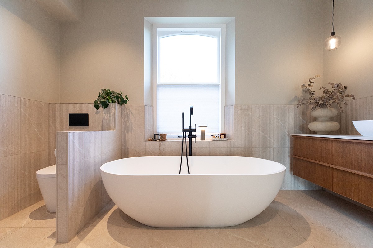 Modern bathroom featuring a white freestanding oval bathtub, floating wooden vanity, and beige wall tiles.