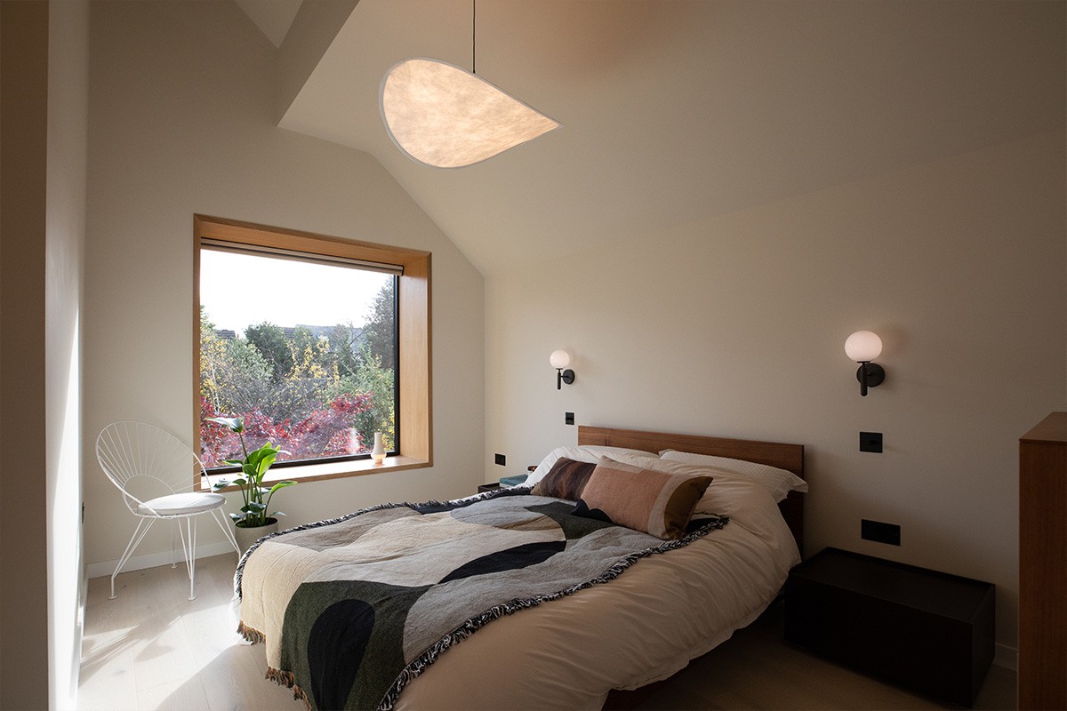 Modern bedroom with a wooden bed, patterned throw blanket, curved paper pendant light, and a large picture window.