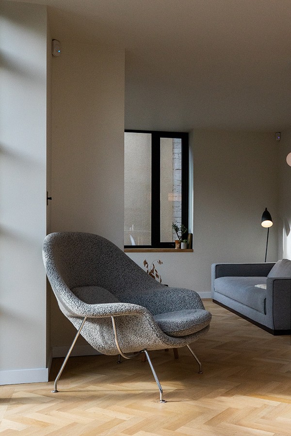 Grey textured bouclé lounge chair with thin chrome legs on a light wood herringbone floor.