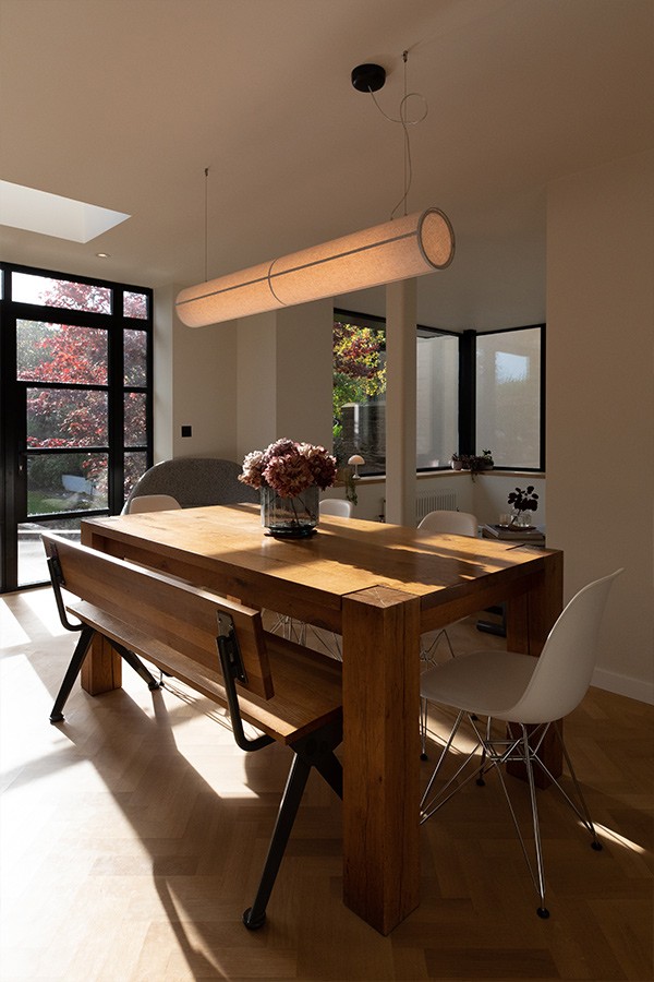 Solid wood dining table paired with a wooden bench and white chairs, illuminated by a cylindrical pendant light.