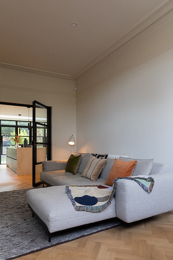Light grey sectional sofa on a textured dark rug with open black glass doors leading into a kitchen.