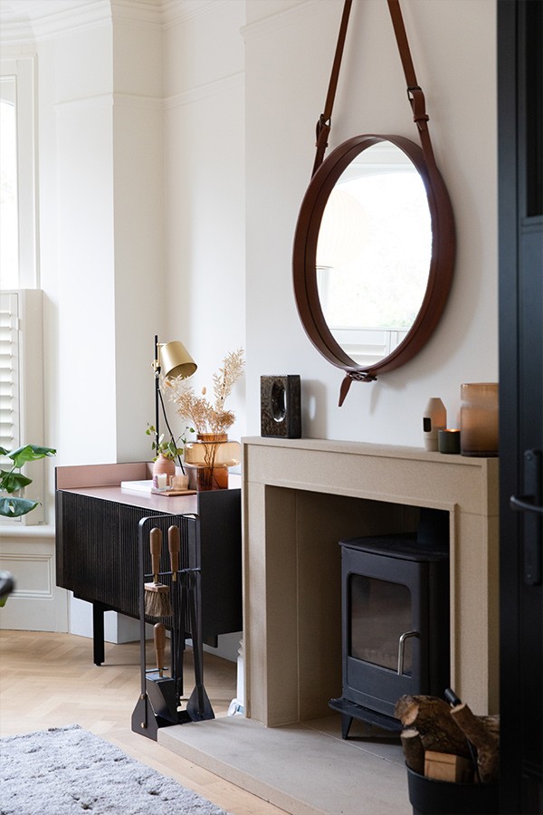 Beige stone fireplace with a wood-burning stove, brown leather mirror, and black fluted sideboard.