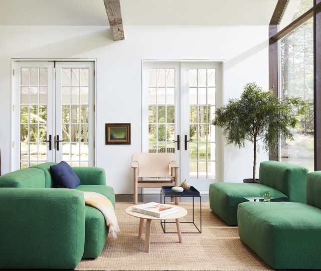 Modern low-profile modular sofa in green fabric, paired with a round light wood coffee table and a beige jute rug in a sunlit living room.