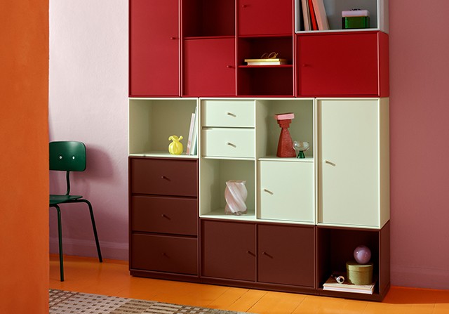 Colourful modular shelving unit featuring red, pale green, and dark brown cabinets and drawers against a pink wall.