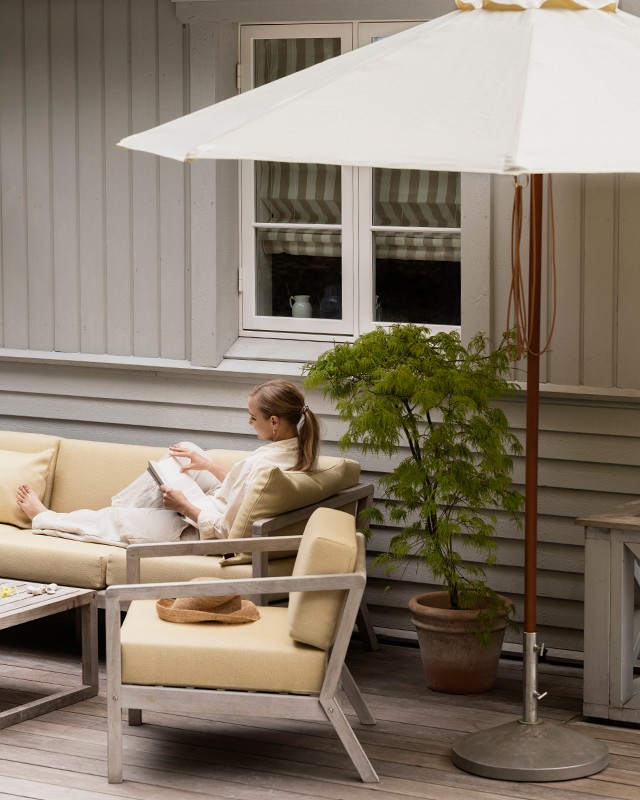 Lady sat relaxing on Skagerak Collection Virkelyst Outdoor Seating shaded with Catania Umbrella