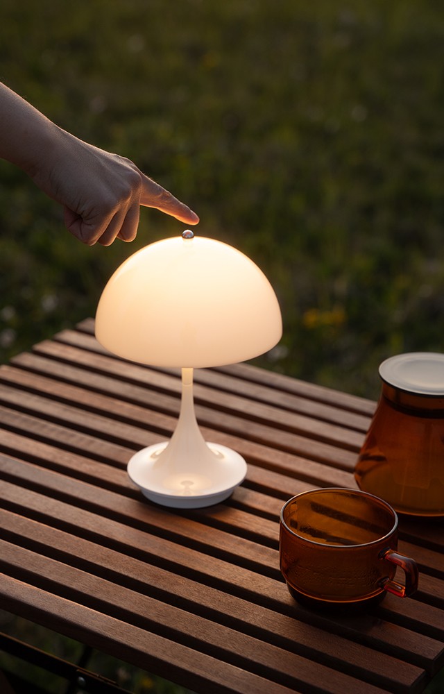 Louis Poulsen 160 Portable Table Lamp V3 opal white in outdoor relaxed setting being turned on 