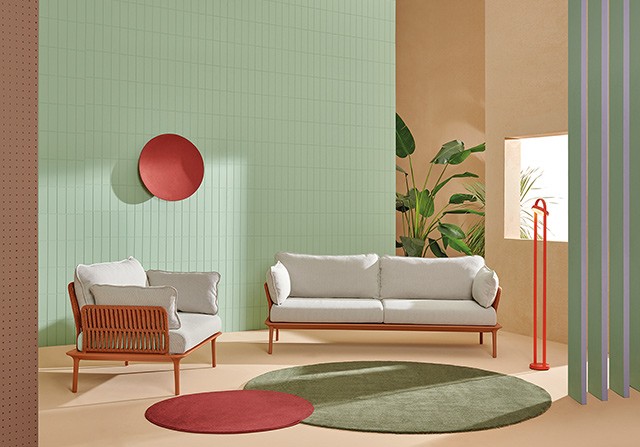 Light grey outdoor sofa and matching armchair with terracotta woven backs, set against a pastel green tiled wall.