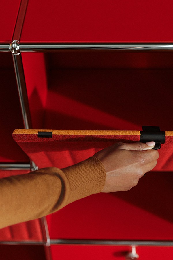 Close up of USM Haller bookcase in red with soft panelling as lady opens a section