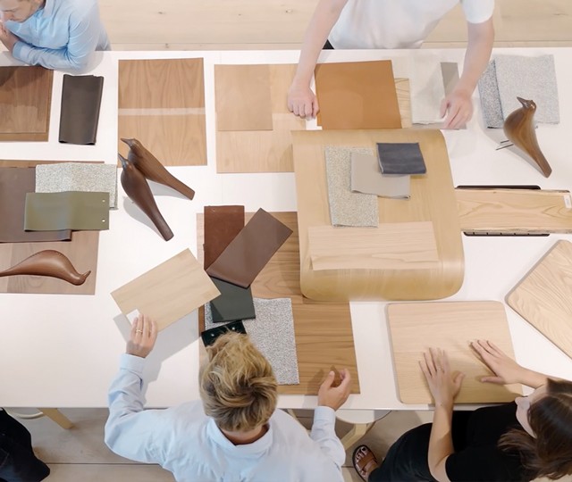 Overhead view of designers arranging wood samples, fabric swatches, leather finish options, and wooden bird sculptures.