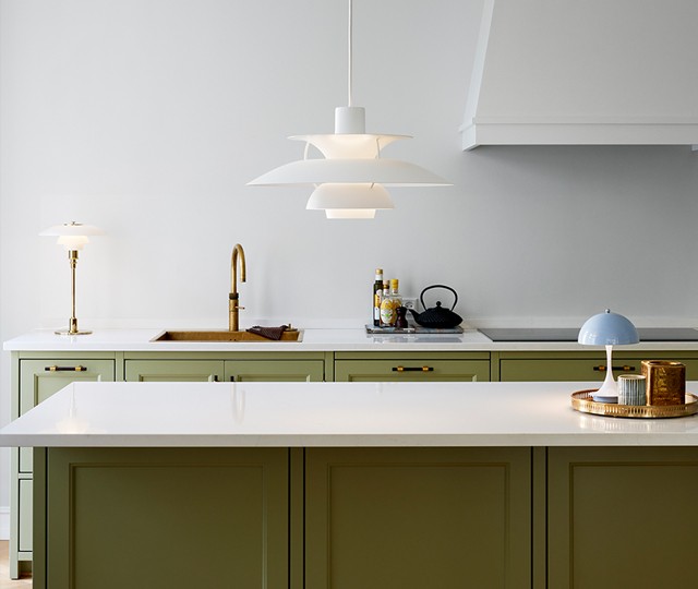 White multi-shaded pendant light hanging over a kitchen island with olive green cabinets, white countertops, and a brass faucet.