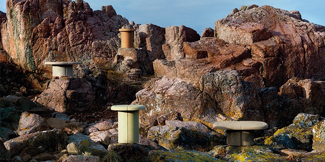Sculptural cylindrical side tables in earth tones placed outdoors among rugged, rocky red cliffs.