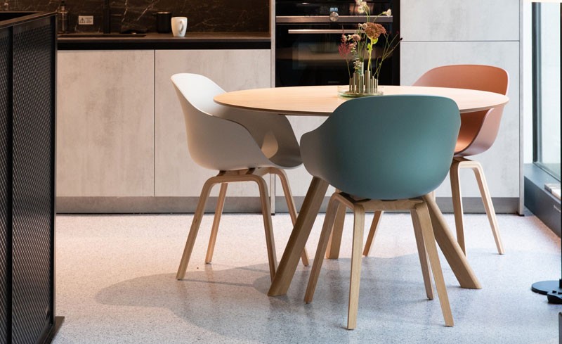 3 plastic dining chairs with wooden legs around a circular wooden table in a modern kitchen